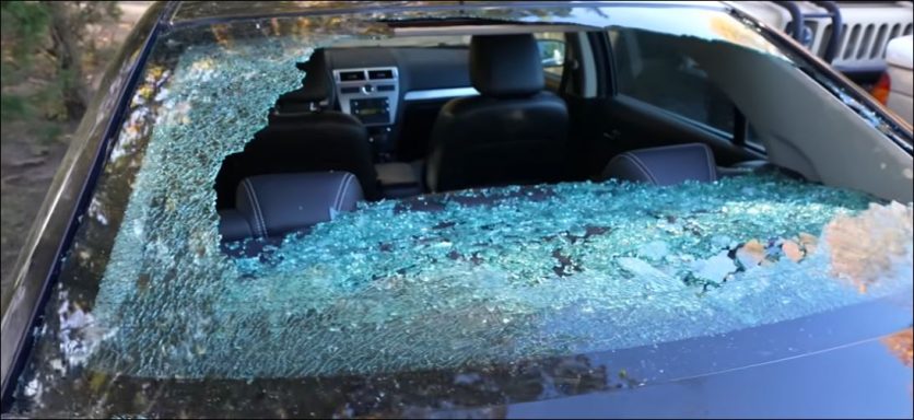 A shattered car window with broken glass scattered inside and outside the vehicle.